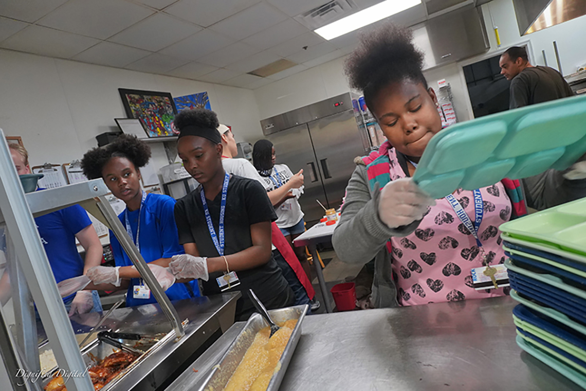 "Image of young Black women working in an industrial kitchen."