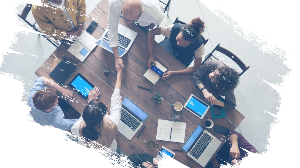 Overhead shot of people gathered around a table on computers and other devices.